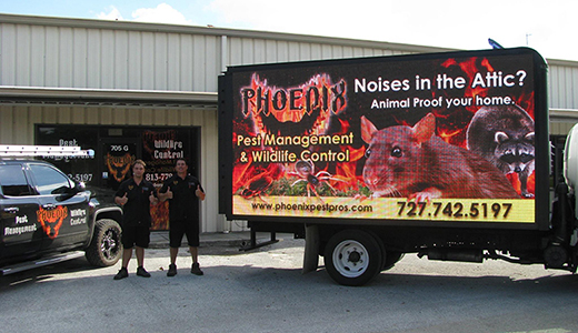 Two Employees of Rat Removal Company Posing Between Company Vehicles In Front of Oldsmar Office